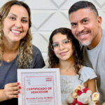 Amanda, sua mãe e seu pai abraçados, segurando a Certificado de Vencedor do IDEARforEARS