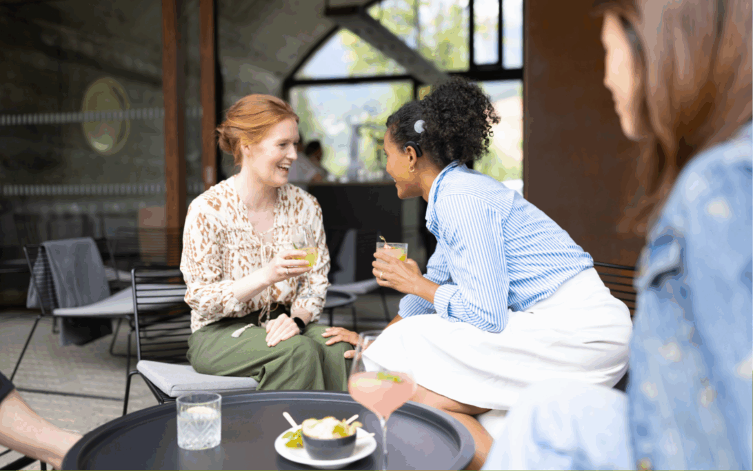 Two young women at a coffee shop talking to each other, one is wearing a cochlear implant