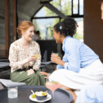 Two young women at a coffee shop talking to each other, one is wearing a cochlear implant