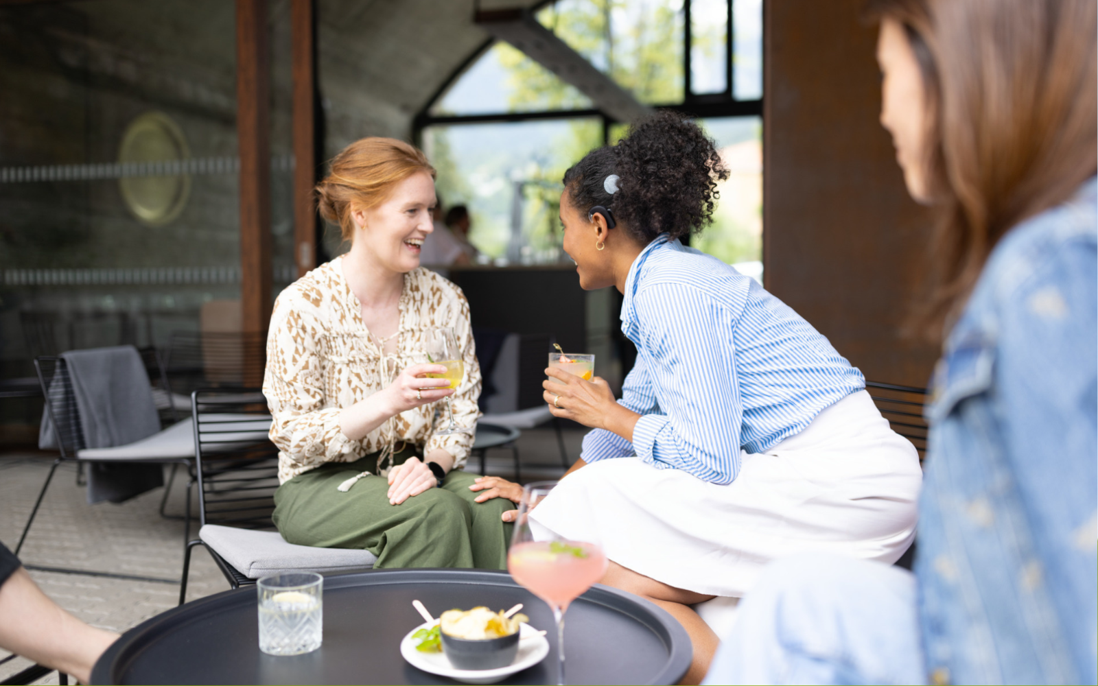 Two young women at a coffee shop talking to each other, one is wearing a cochlear implant