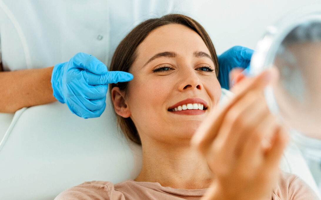 A woman at a cosmetic procedure, looking into the mirror with a smile