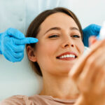 A woman at a cosmetic procedure, looking into the mirror with a smile
