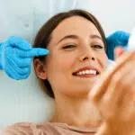 A woman at a cosmetic procedure, looking into the mirror with a smile