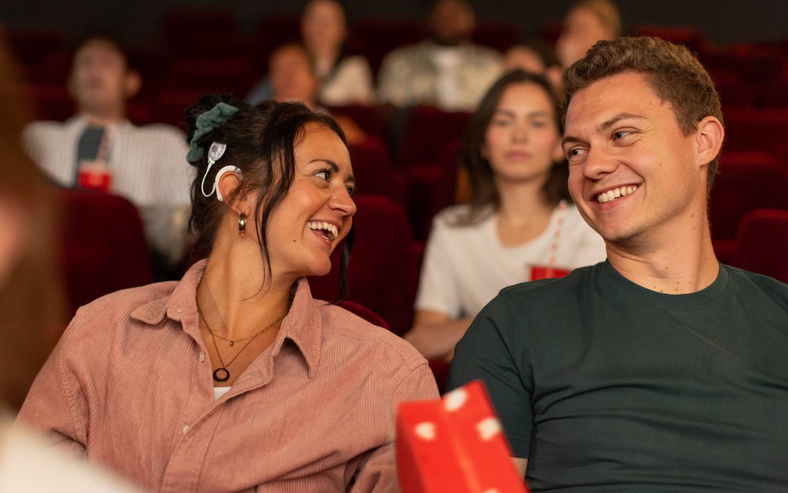A couple sit in a cinema. The woman has an audio processor.