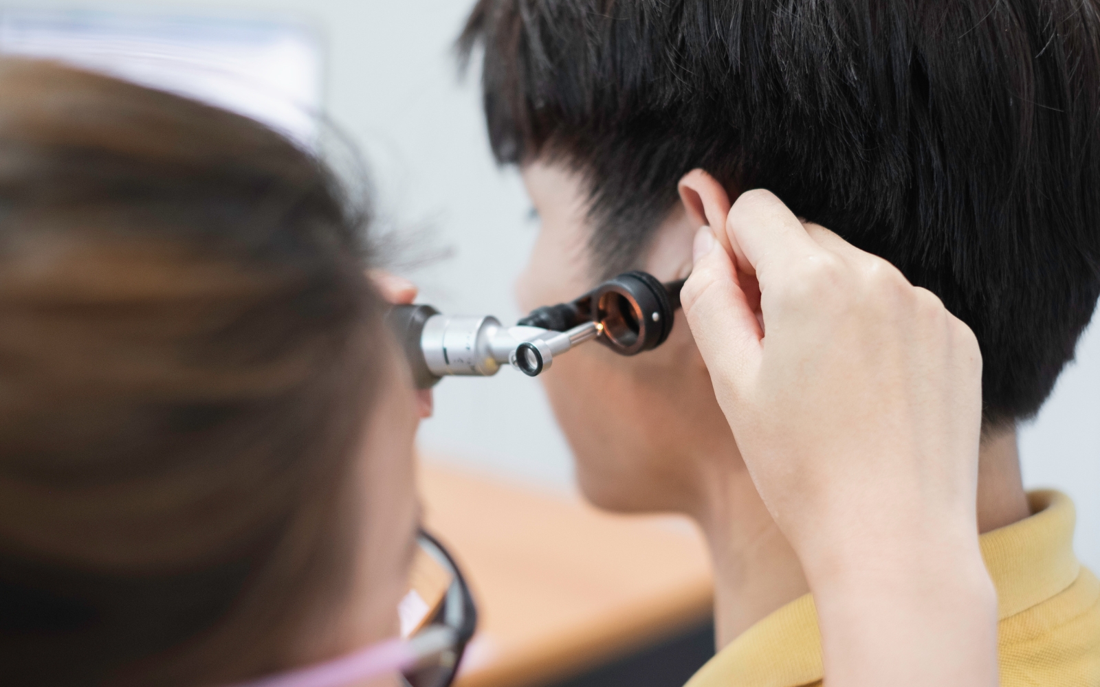 Profissional examinando o canal auditivo de uma pessoa com um otoscópio durante avaliação de possível perda auditiva.