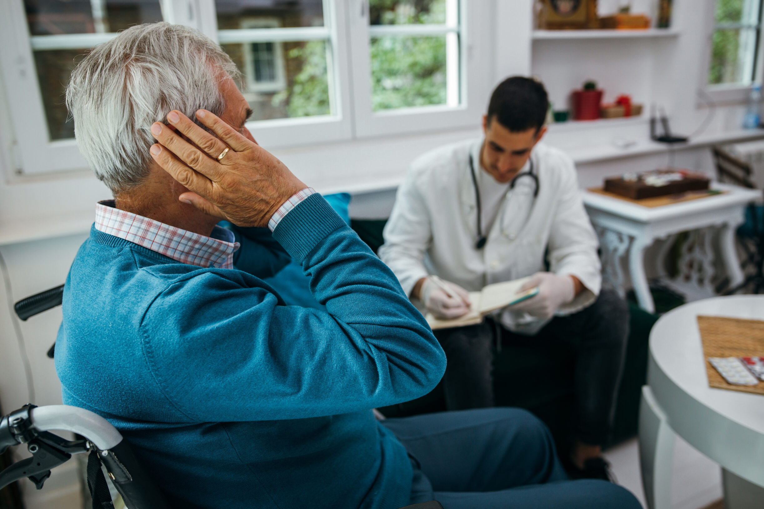 Young doctor talks with a patient who complains of earache during home visit.