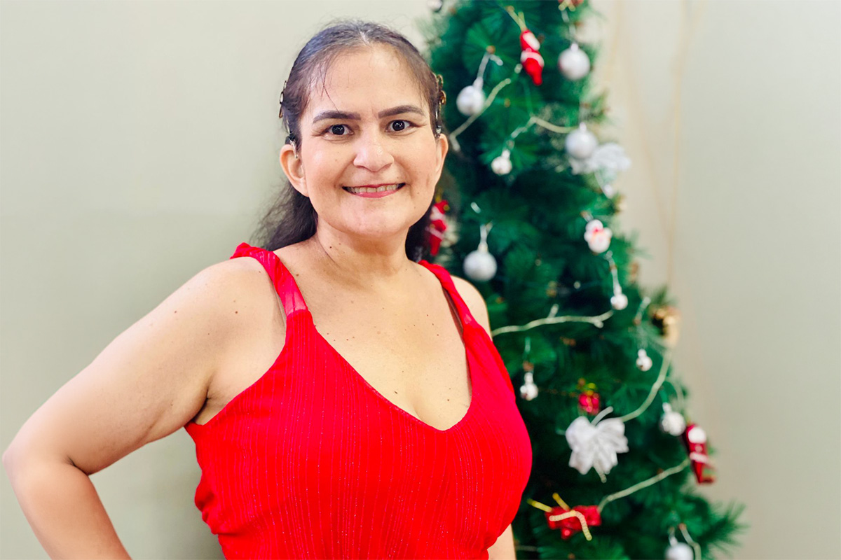 Karine usando vestido vermelho, com árvore de Natal ao fundo.