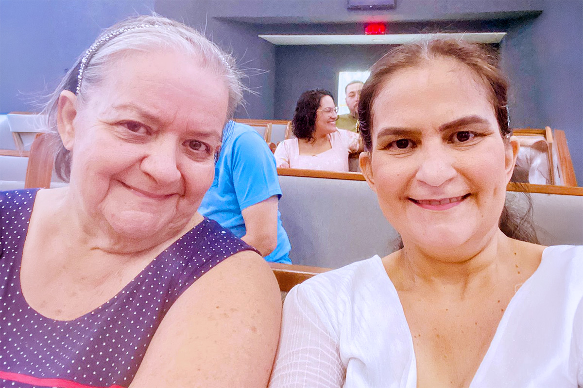 Karine sentada em banco de igreja ao lado de sua mãe.