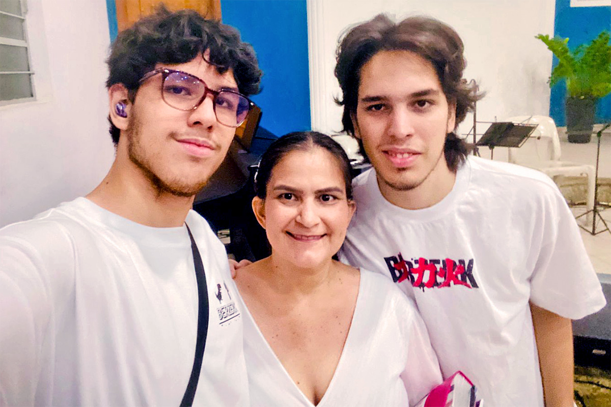 Karine e seus filhos em ambiente interno, com instrumentos musicais ao fundo.