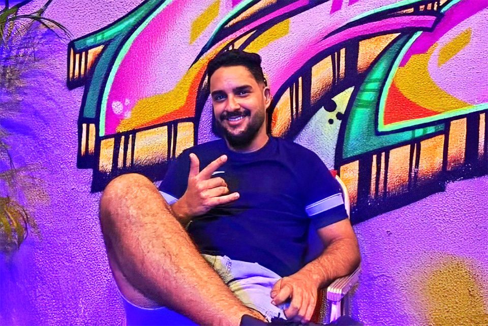 Arthur sentado em cadeira, diante de mural grafitado colorido.