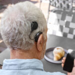 Ein Mann mit Cochlea-Implantat sitzt beim Frühstück und schaut auf sein Handy