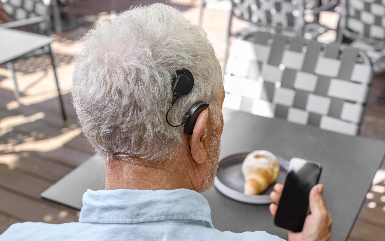 Ein Mann mit Cochlea-Implantat sitzt beim Frühstück und schaut auf sein Handy