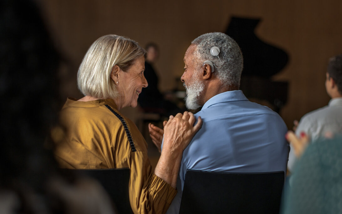 A man with a cochlear implant speaking to a woman next to him at a concert