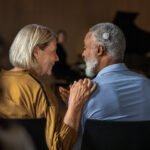 A man with a cochlear implant speaking to a woman next to him at a concert
