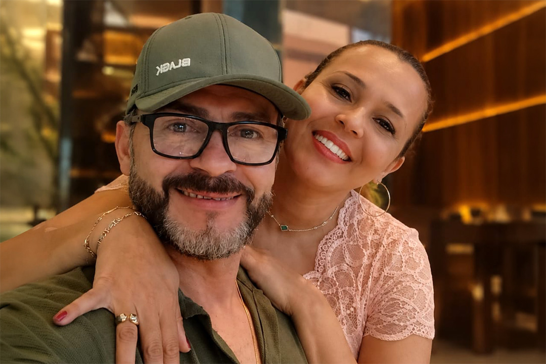 Maria Angélica ao lado do marido em ambiente interno, registrada durante momento compartilhado do cotidiano.